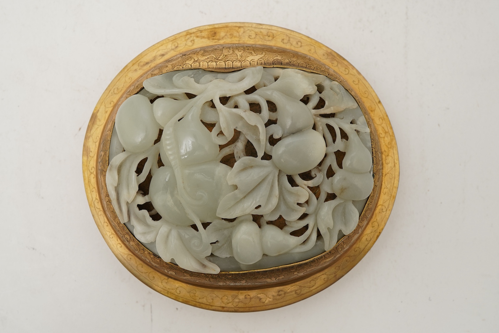 A Chinese pale celadon jade oval plaque, 17th/18th century, mounted on a late Qing gilt copper jar